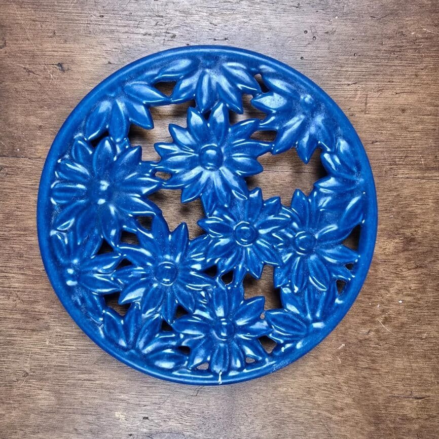 Dessous de plat en fonte émaillée bleue à fleurs Invicta vue de dessus sur table en bois