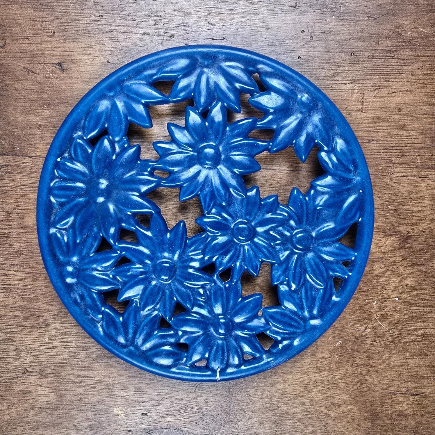 Dessous de plat en fonte émaillée bleue à fleurs Invicta vue de dessus sur table en bois
