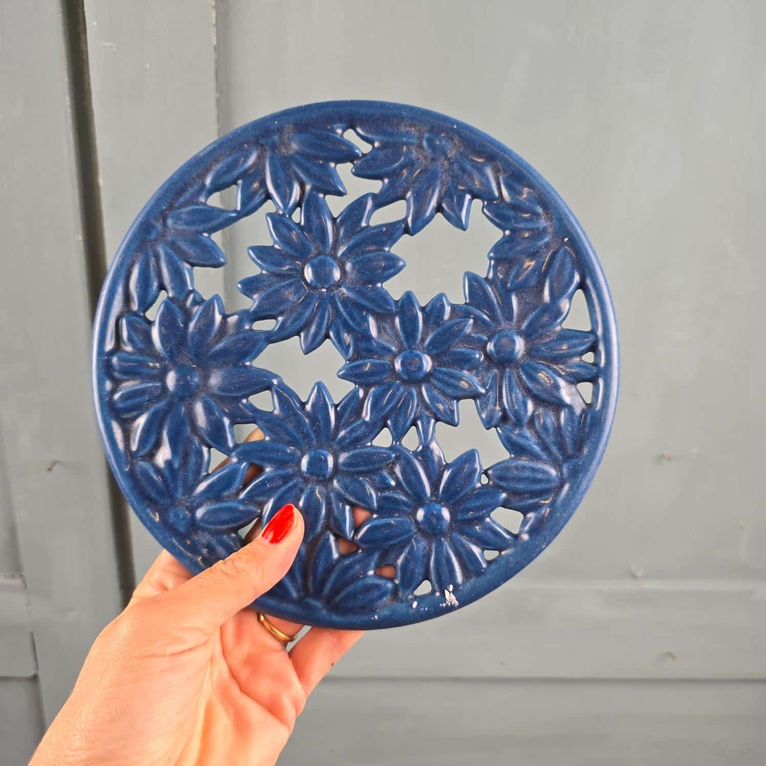 Dessous de plat en fonte émaillée bleue à fleurs Invicta tenu en main pour mesure