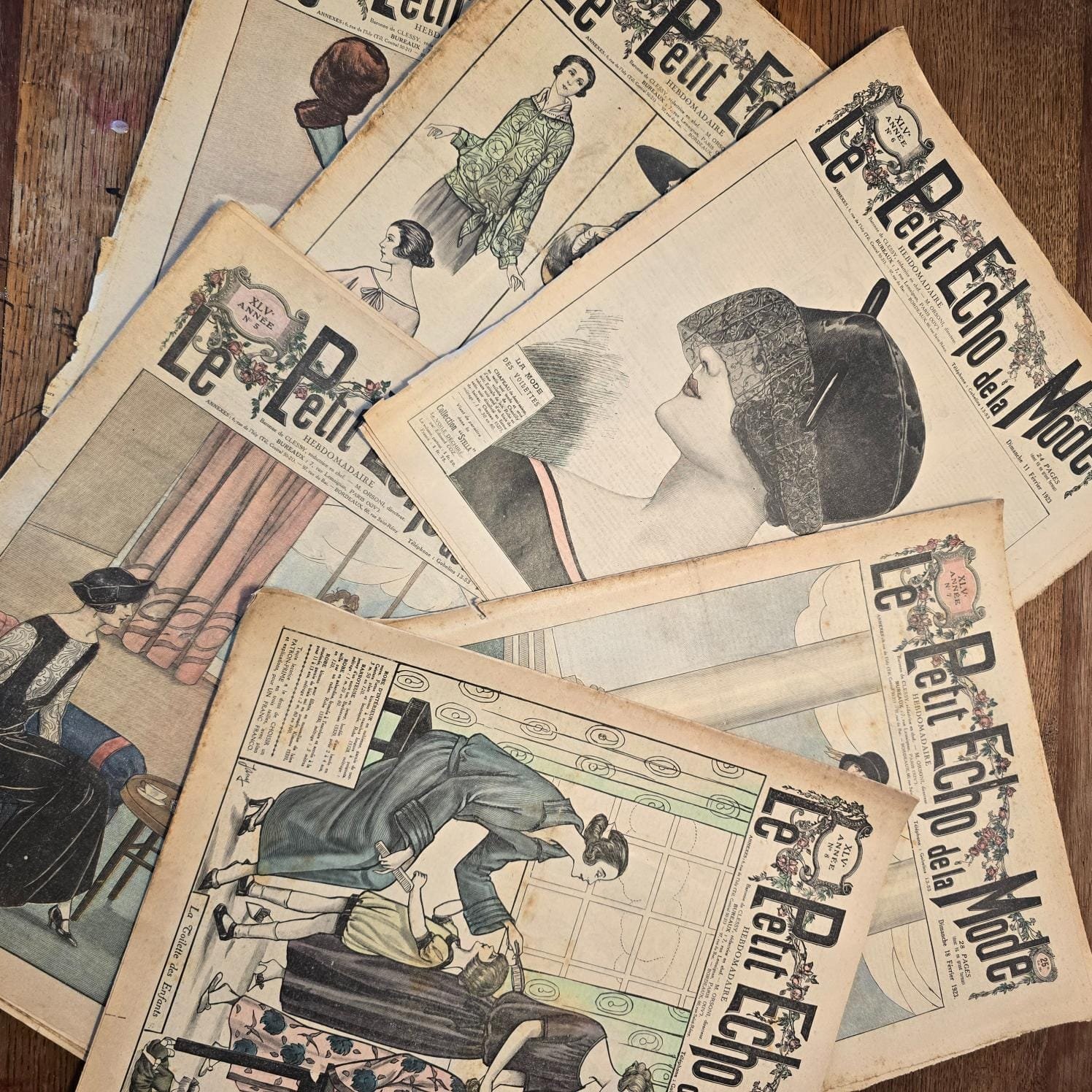 Ensemble de magazines « Le Petit Écho de la Mode » étalés sur table en bois, vue de dessus