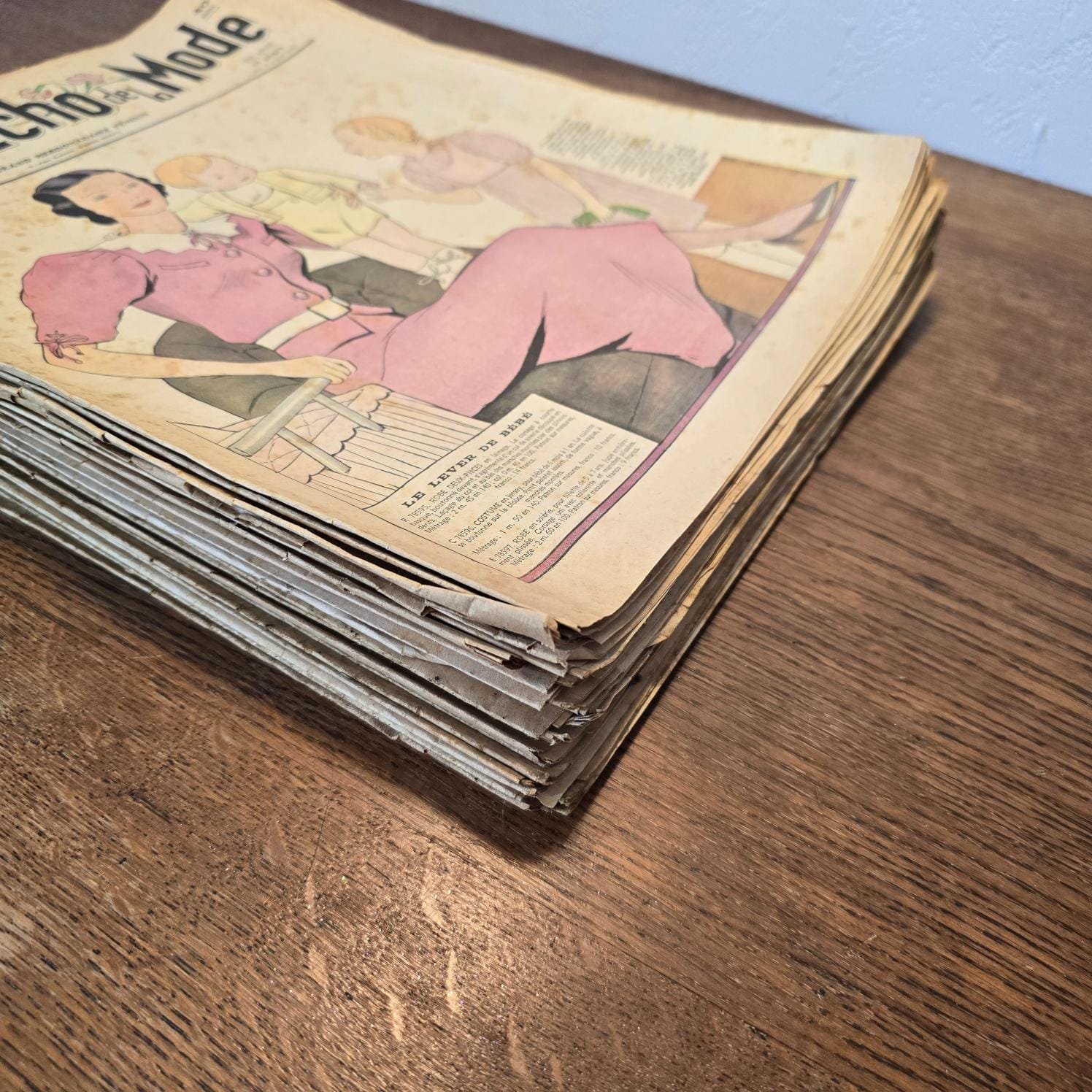Lot de 30 « Le Petit Écho de la Mode », 1936, magazines posés en tas sur une table en bois, montrant la conservation de ces magazines
