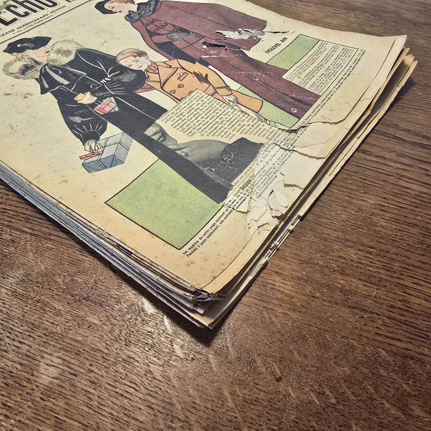Lot de 13 « Le Petit Écho de la Mode », 1935 – Magazines anciens illustrés posés en tas sur table en bois montrant les déchirures et coupures dans les magazines