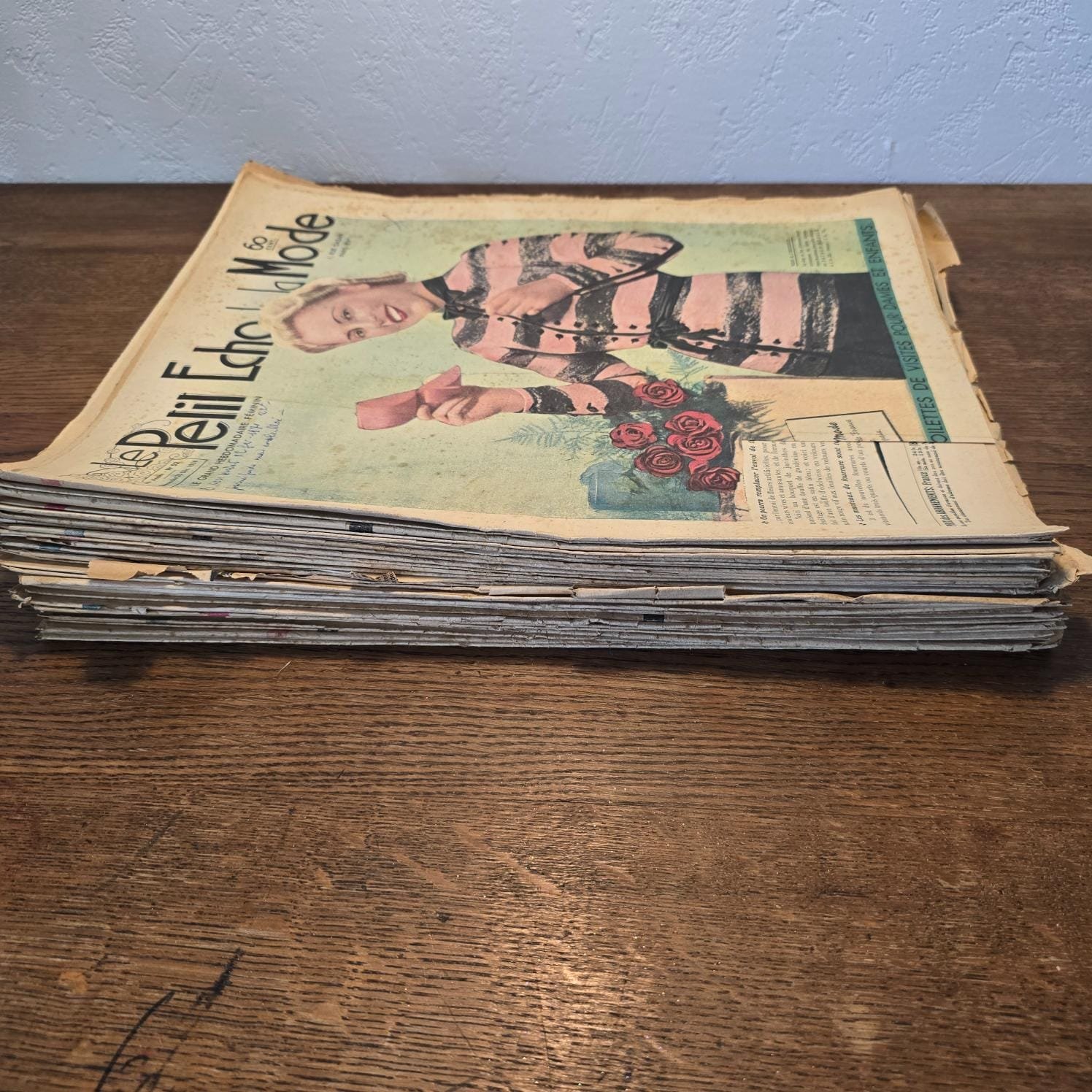 Lot de 35 « Le Petit Écho de la Mode » de 1938, en tas sur une table en bois, vue de côté