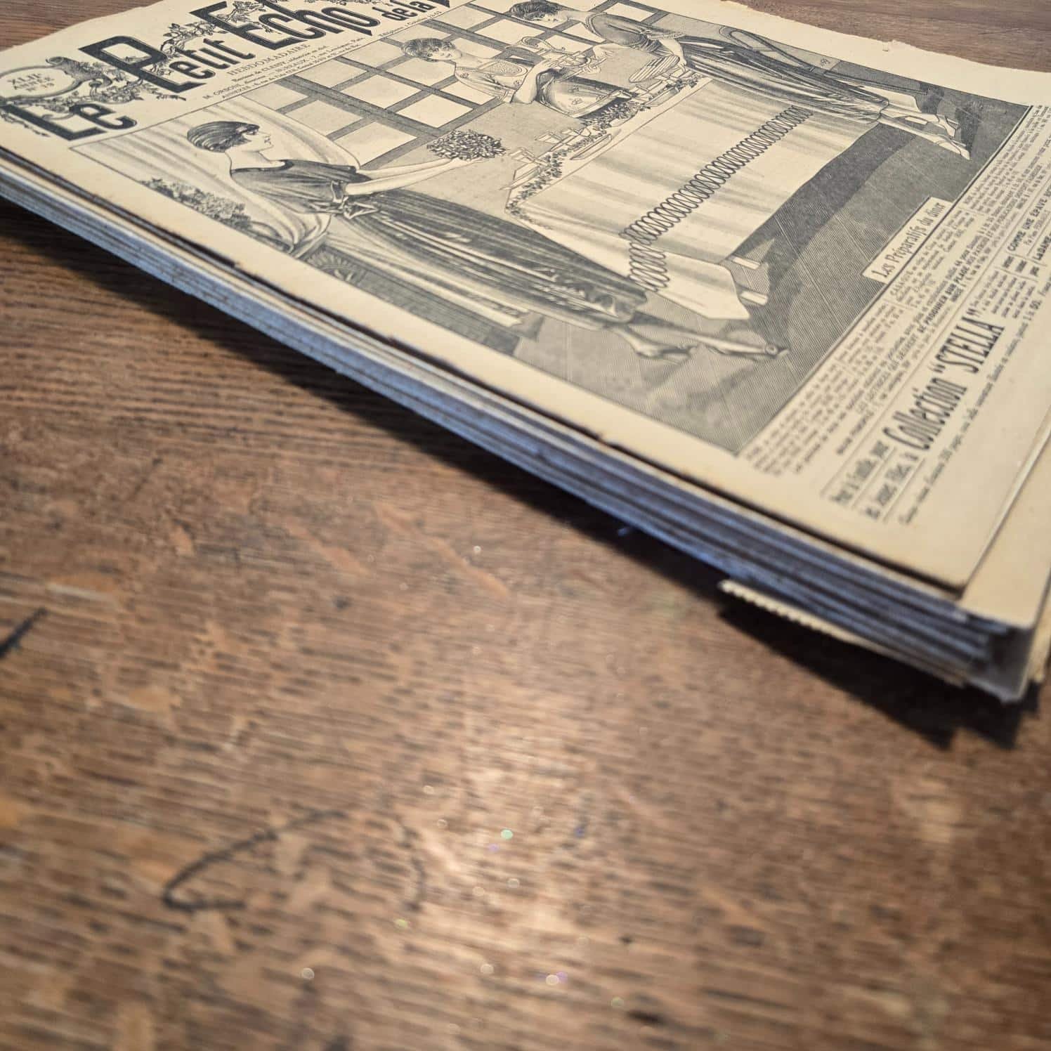Ensemble de magazines « Le Petit Écho de la Mode » des années 30, posés en tas sur table en bois, vue de côté