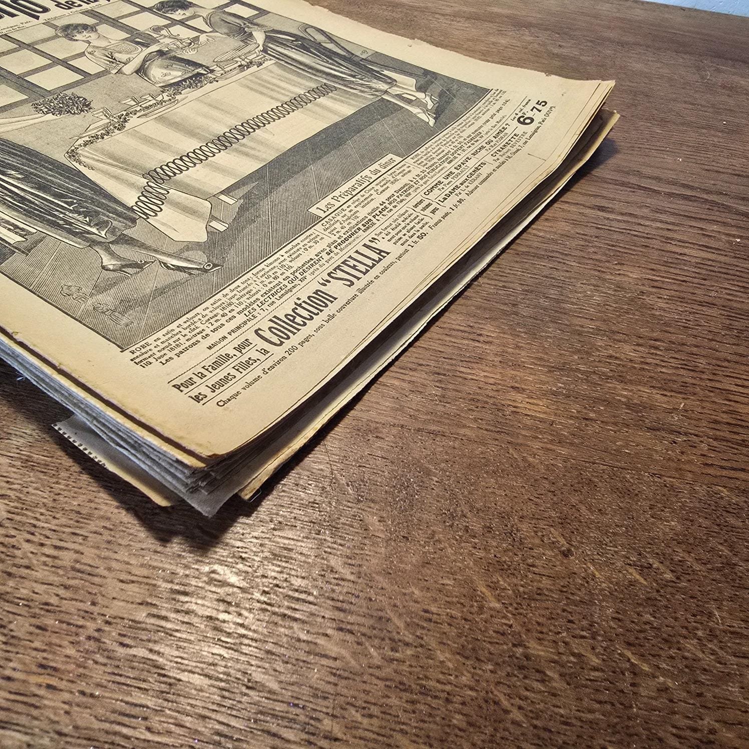 Ensemble de magazines « Le Petit Écho de la Mode » des années 30, posés en tas sur table en bois, vue plongeante sur la tranche basse des magazines