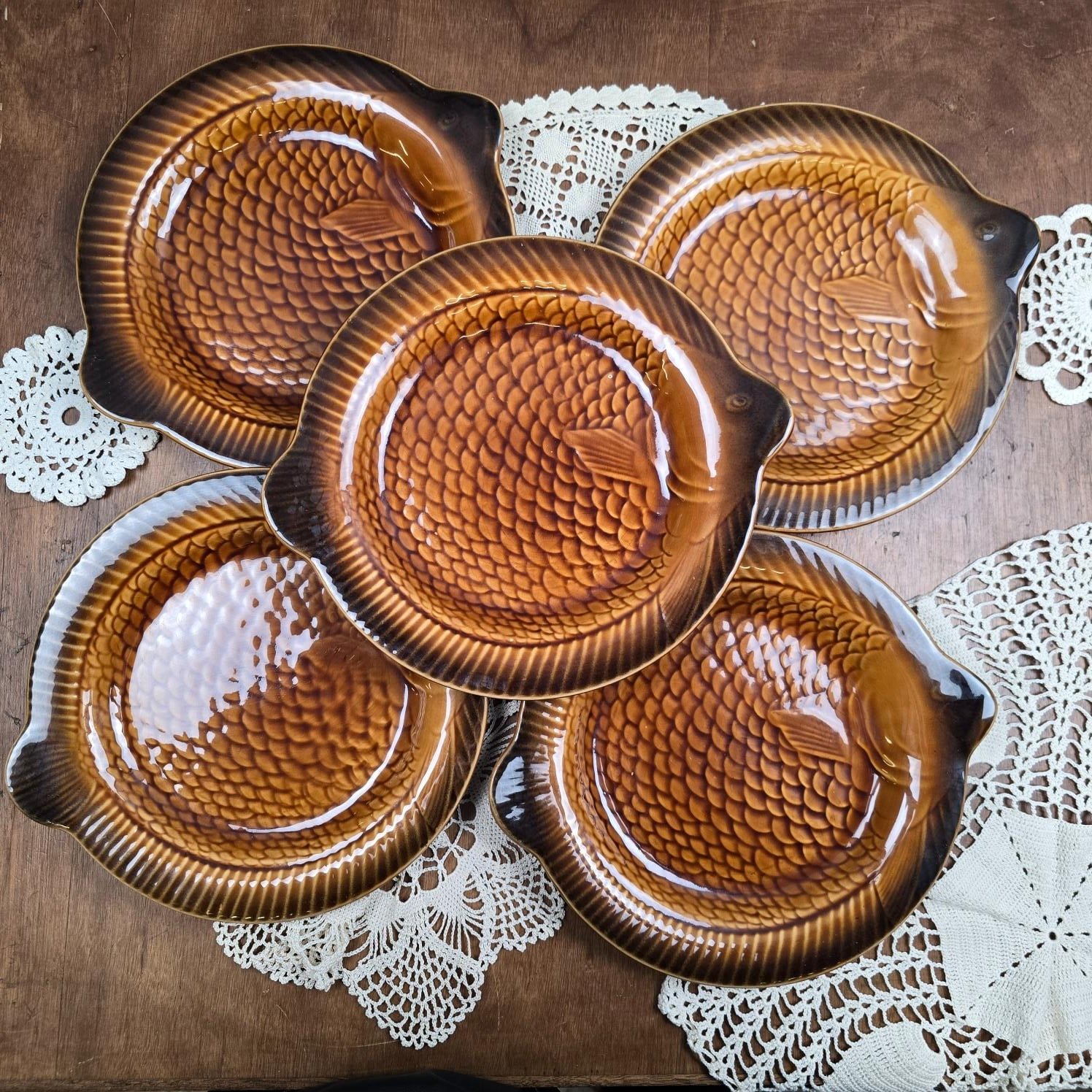 Lot de cinq assiettes poisson Sarreguemines en faïence caramel, disposées sur une nappe en dentelle