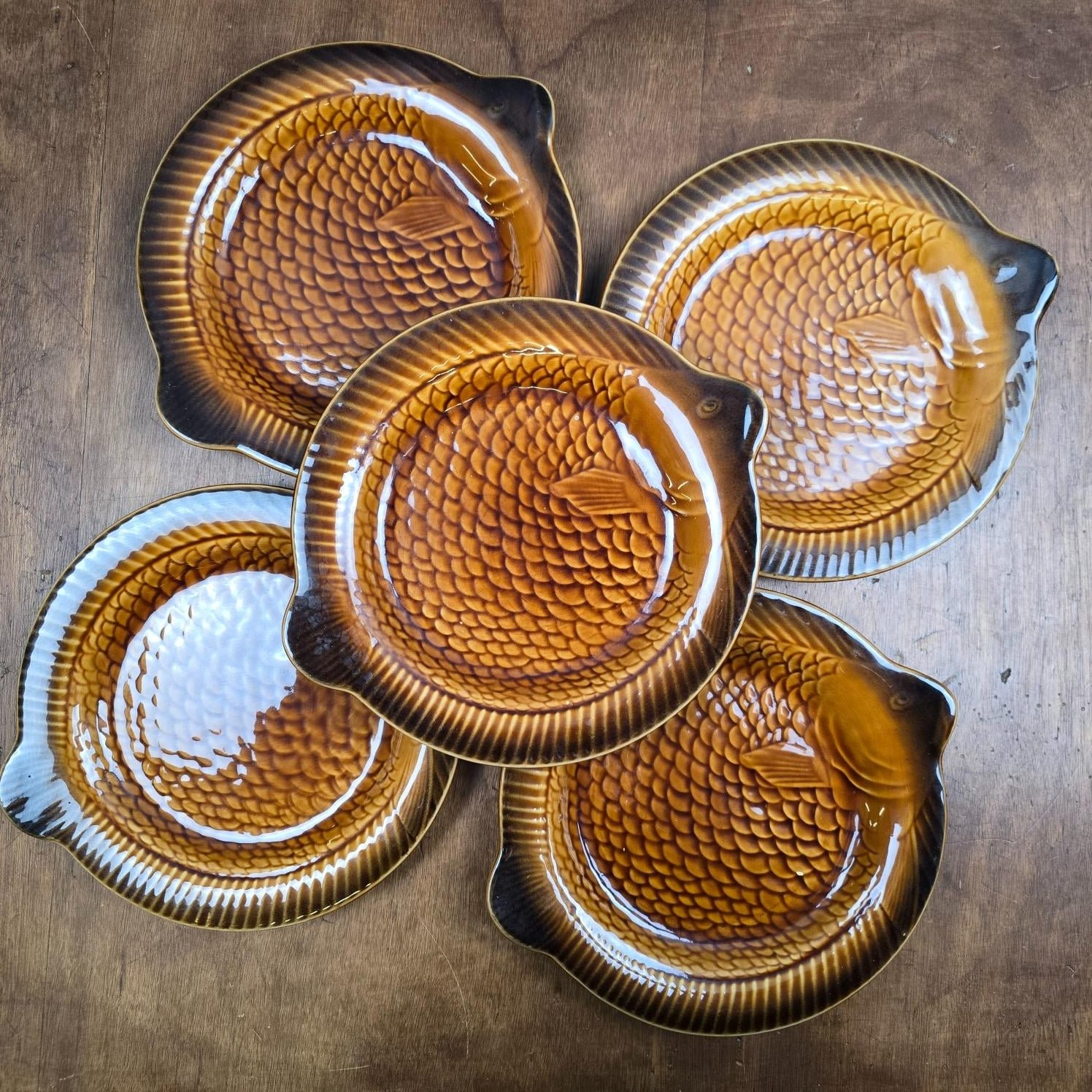 Ensemble de cinq assiettes poisson Sarreguemines marron glacé présenté sur une table en bois