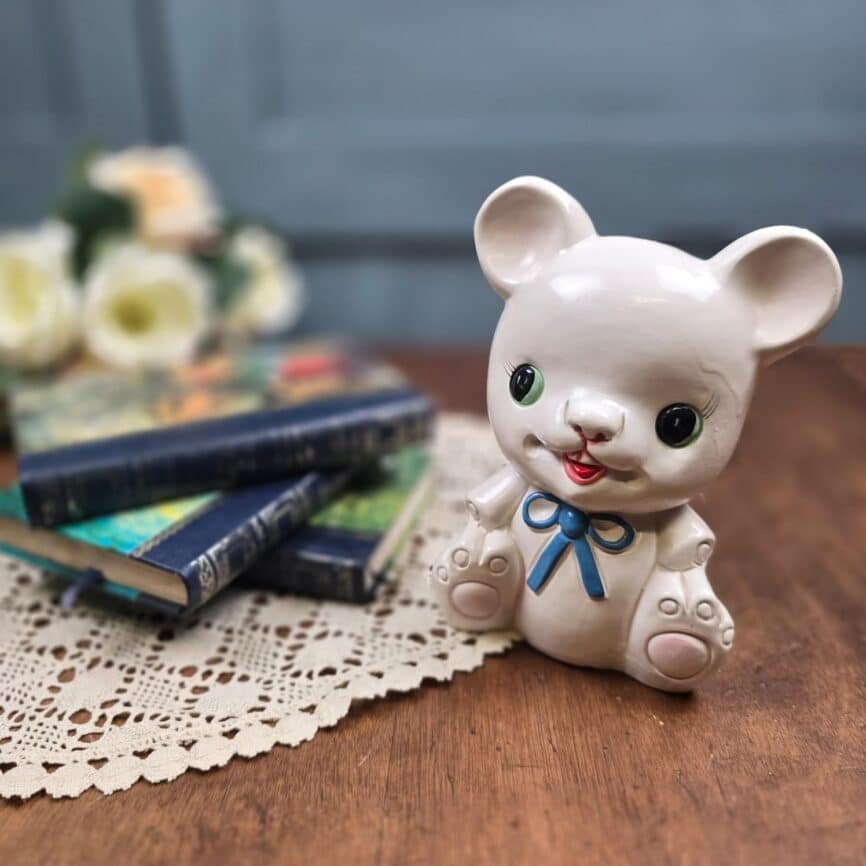 Tirelire ours vintage en céramique blanche avec nœud bleu, mise en scène sur une table avec des livres anciens