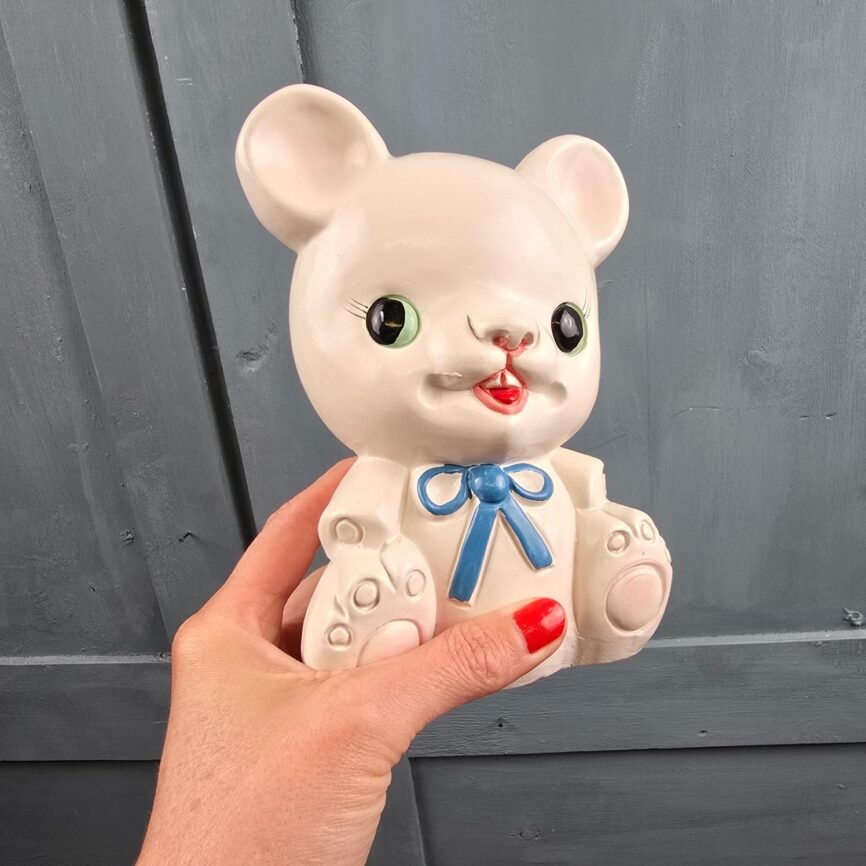 Tirelire nounours blanche aux yeux verts et ruban bleu, tenue en main de trois quarts
