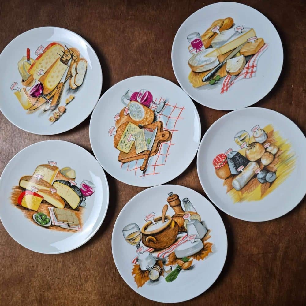 Vue d’ensemble des 6 assiettes à fromage en porcelaine de Brémaille, décor fromages et vins, posées sur table en bois