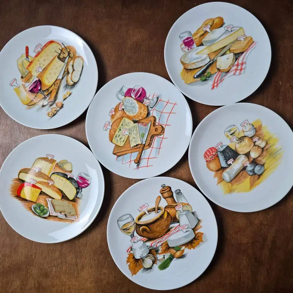 Vue d’ensemble des 6 assiettes à fromage en porcelaine de Brémaille, décor fromages et vins, posées sur table en bois