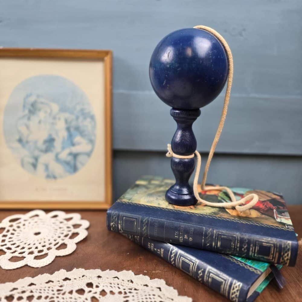 Bilboquet posé sur des livres anciens, corde visible, ambiance déco vintage.