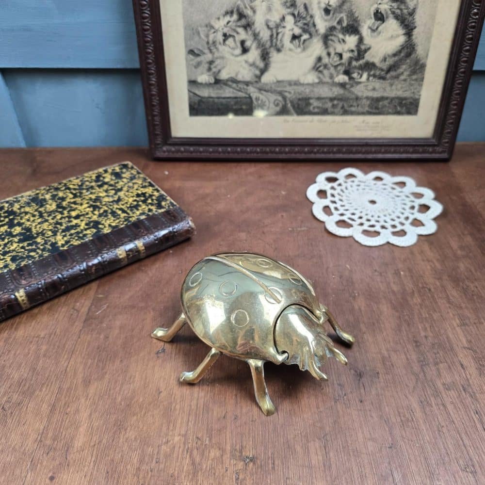Boîte vide-poche vintage en forme de coccinelle en laiton, posée sur une table en bois.