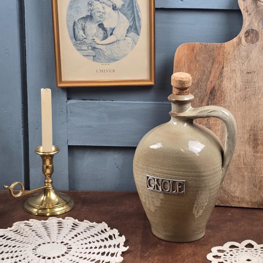 Bouteille ancienne en grès beige « Gnole » posée sur table en bois, ambiance vintage