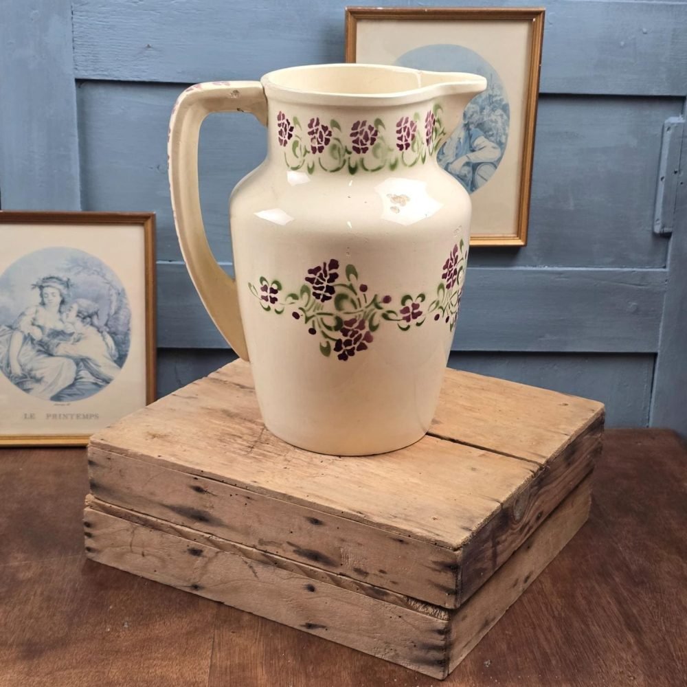 Broc ancien Choisy-le-Roi en terre de fer avec décor floral violet et vert posé sur caisse en bois.