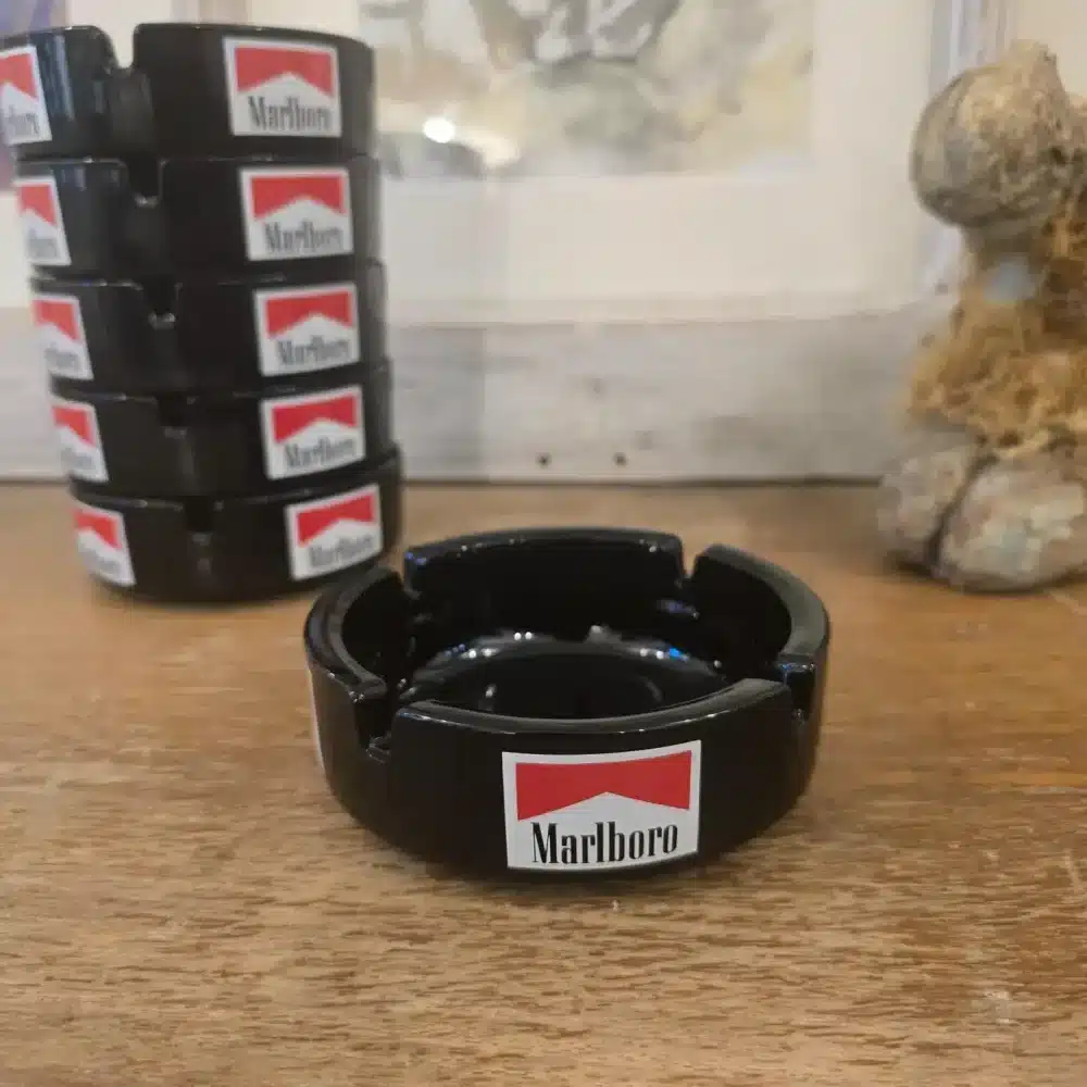 Lot de cendriers publicitaires Marlboro noirs empilés sur table en bois, ambiance vintage