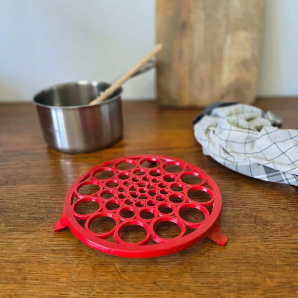 Dessous de plat vintage rouge en situation, sous une casserole, posé sur une table en bois – accessoire pratique et décoratif
