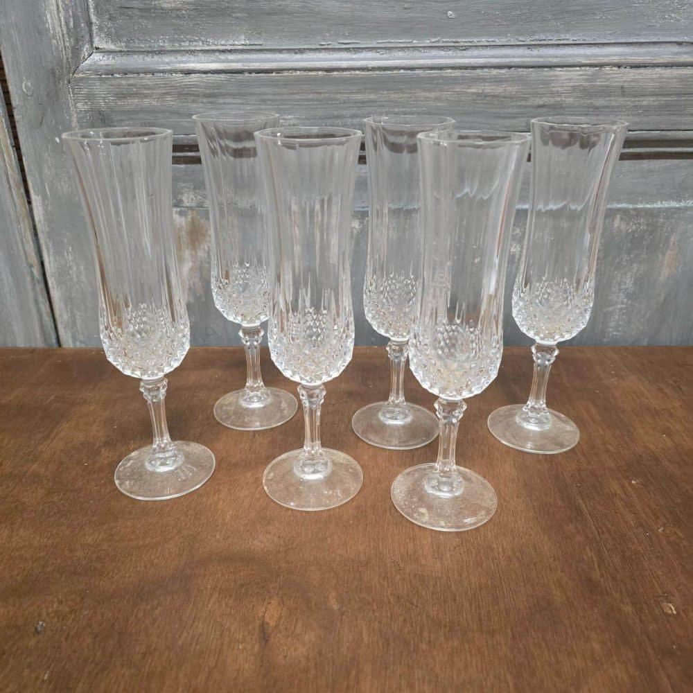 Lot de 6 flûtes à champagne vintage en verre transparent, décor ciselé, posées sur table bois.