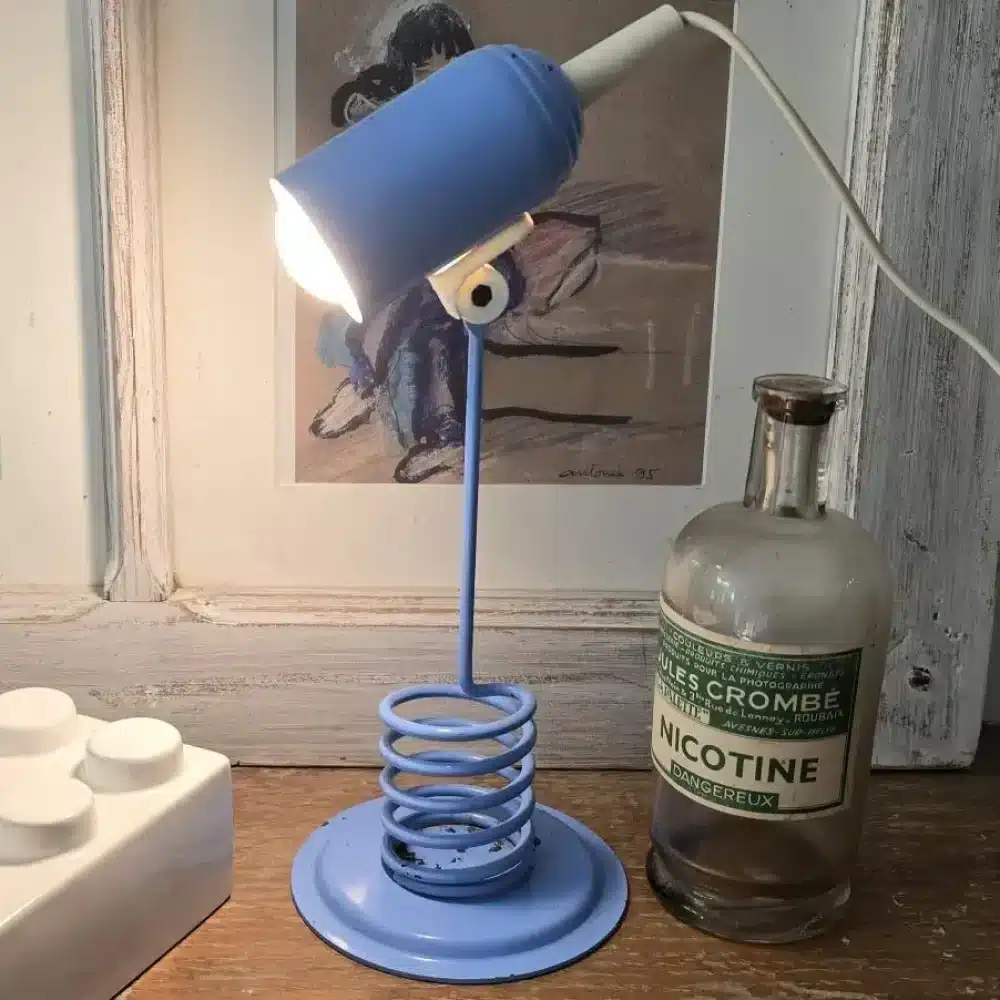 Lampe Space Age vintage en métal bleu avec pied spiralé dans un décor stylisé, lampe allumée.