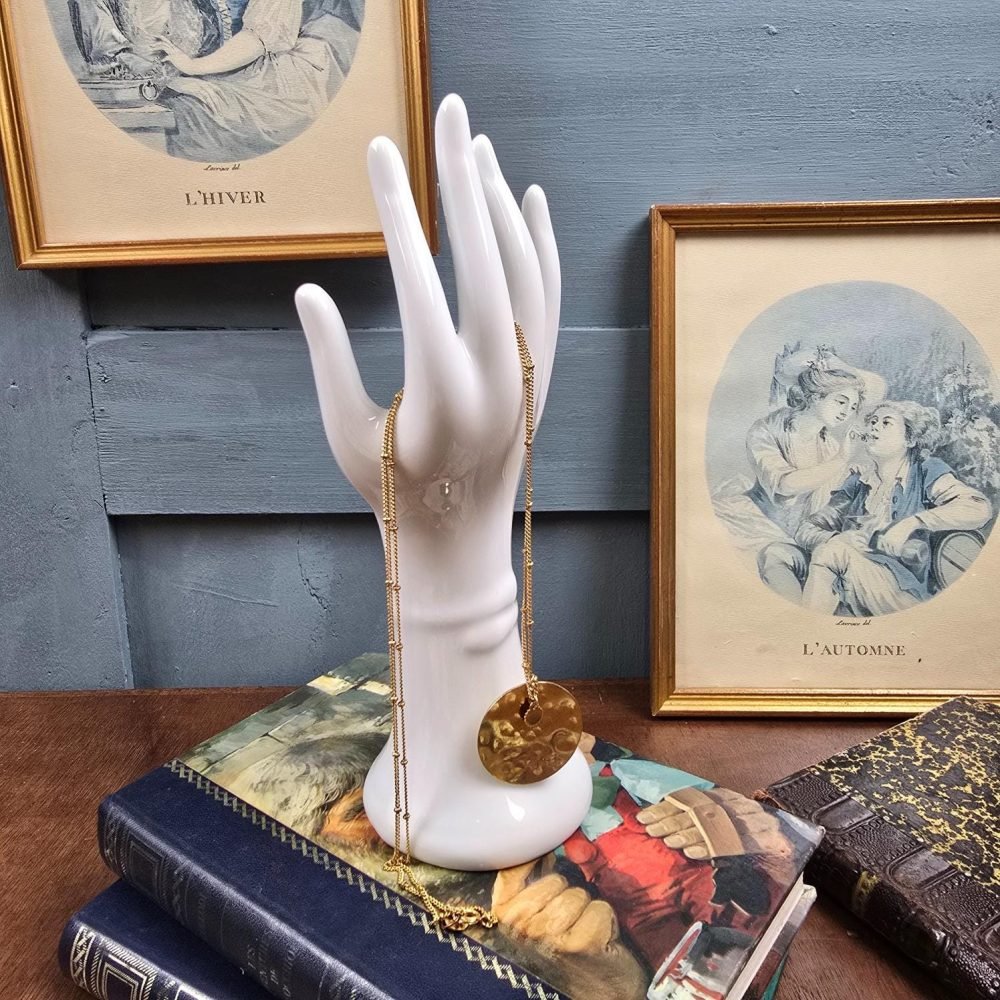 Baguier en porcelaine blanche en forme de main, présenté avec un collier doré.