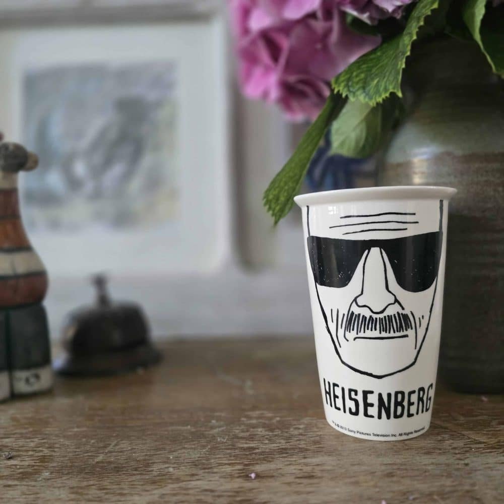 Mug Heisenberg présenté debout sur une table en bois avec une fleur en arrière-plan.