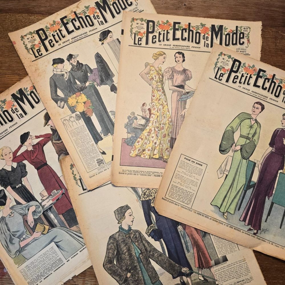 Lot de 13 « Le Petit Écho de la Mode », 1935 – Magazines anciens illustrés étalés sur une table en bois mettant en avant les jolies tenus colorées des couvertures