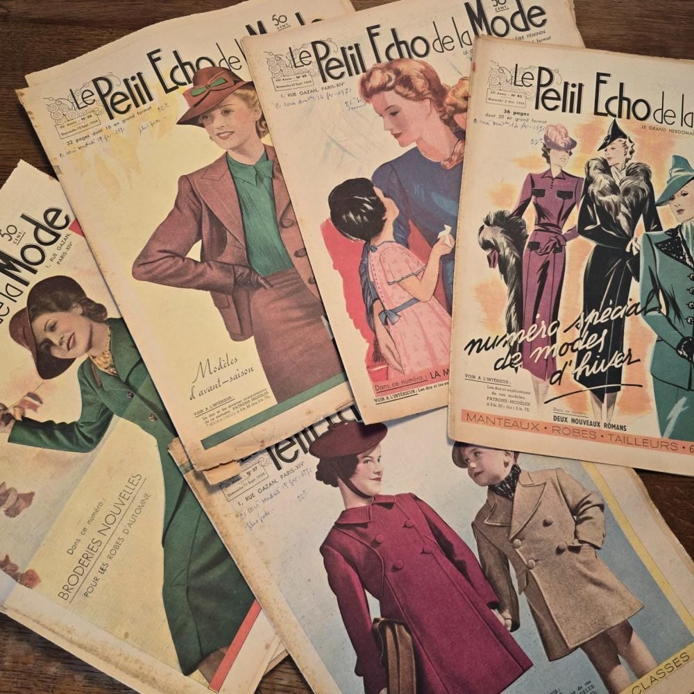 Magazines « Le Petit Écho de la Mode » de 1938, posés sur table en bois avec le numéro spécial de modes d'hiver