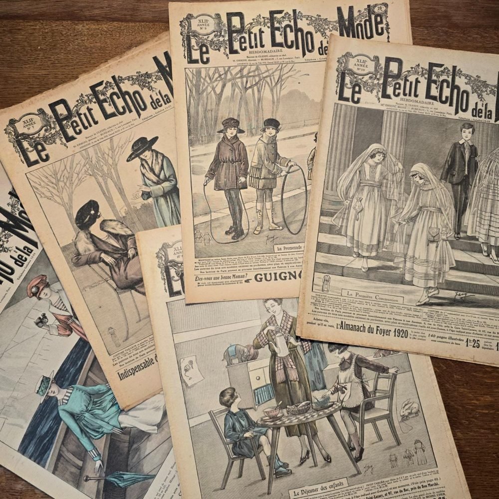 Ensemble de magazines « Le Petit Écho de la Mode » étalés sur table en bois, vue de dessus, couvertures en noir & blanc