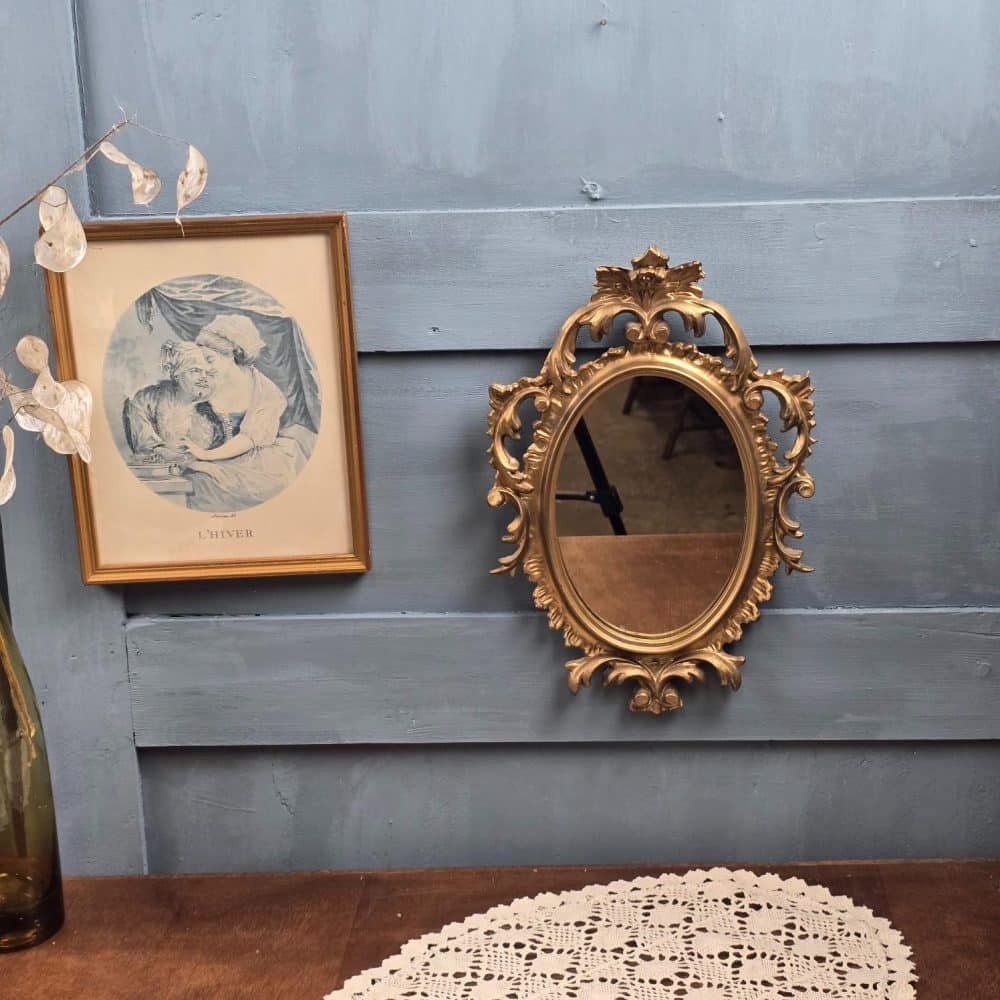 Miroir baroque doré accroché au mur, cadre rocaille.