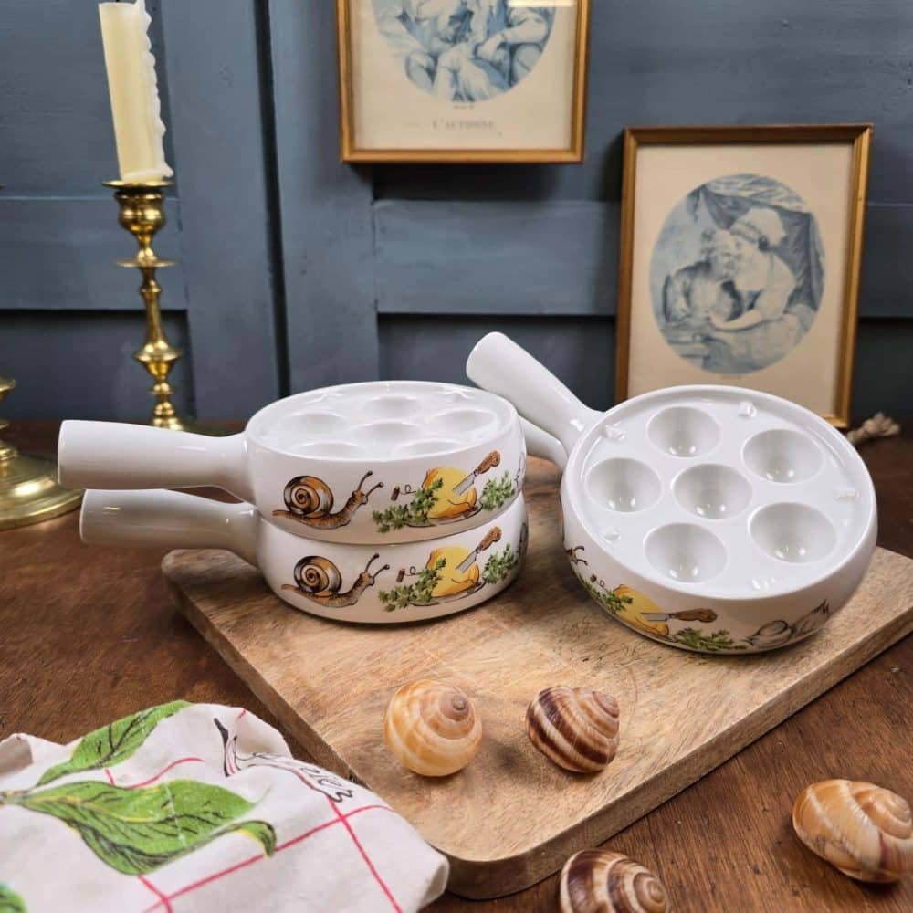 Présentation du lot de 4 poêlons à escargots en porcelaine L’Hirondelle, décor escargots, posés en scène sur une table vintage.