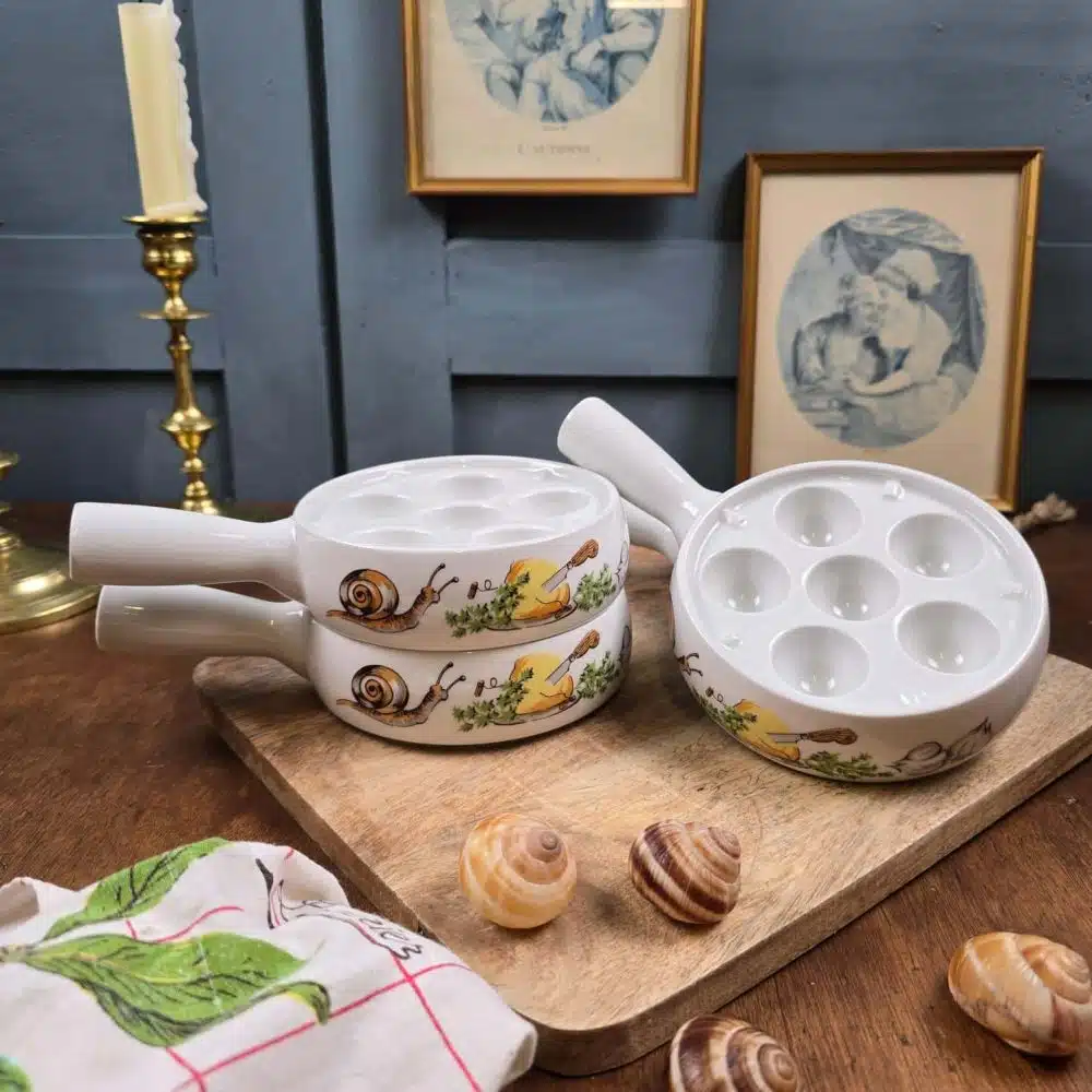 Présentation du lot de 4 poêlons à escargots en porcelaine L’Hirondelle, décor escargots, posés en scène sur une table vintage.