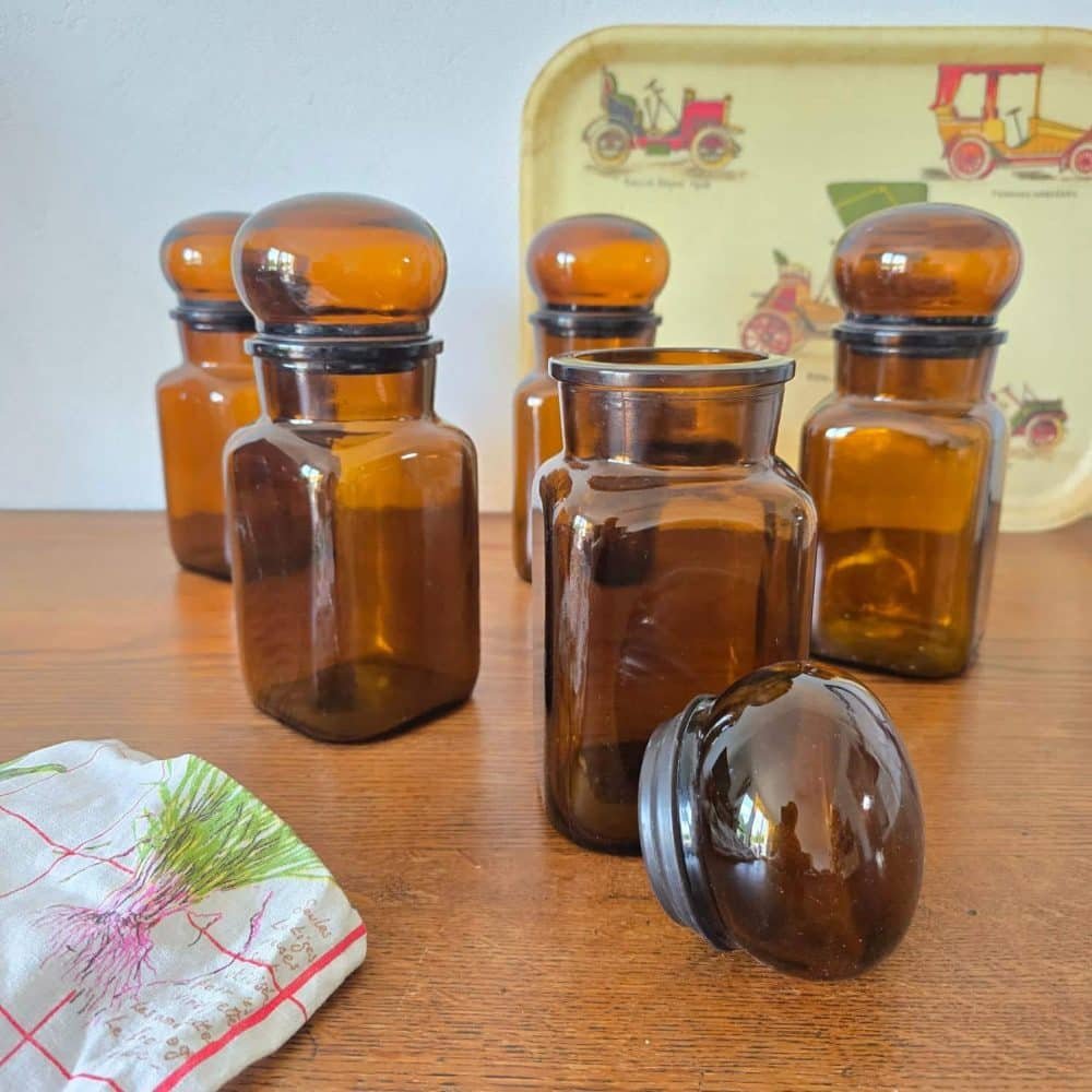 Ensemble de pots en verre ambré Jacques Vabre posés sur table bois, couvercle sur le côté