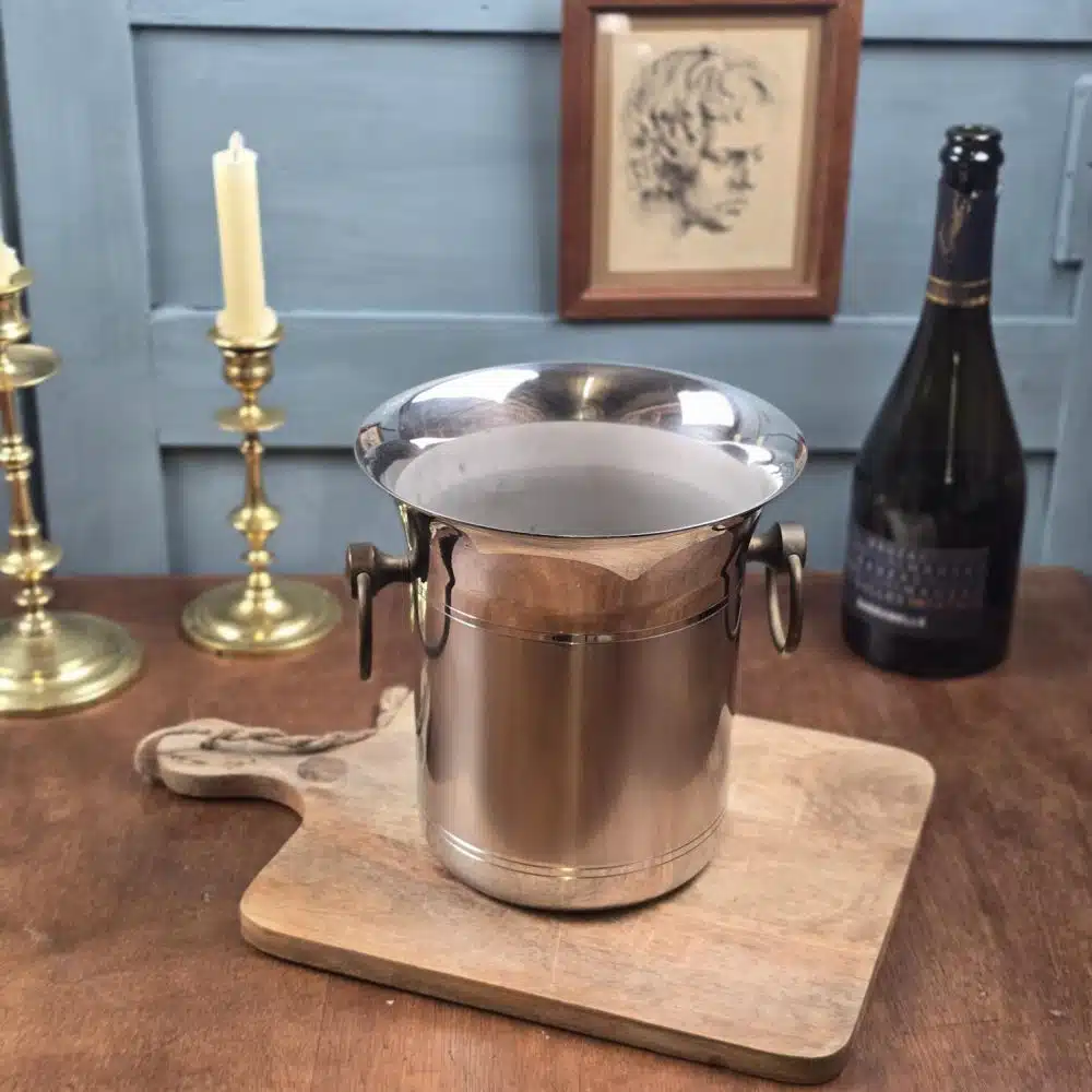 Seau à champagne Jean Couzon en inox 18/10 posé sur planche en bois, anses en anneaux.
