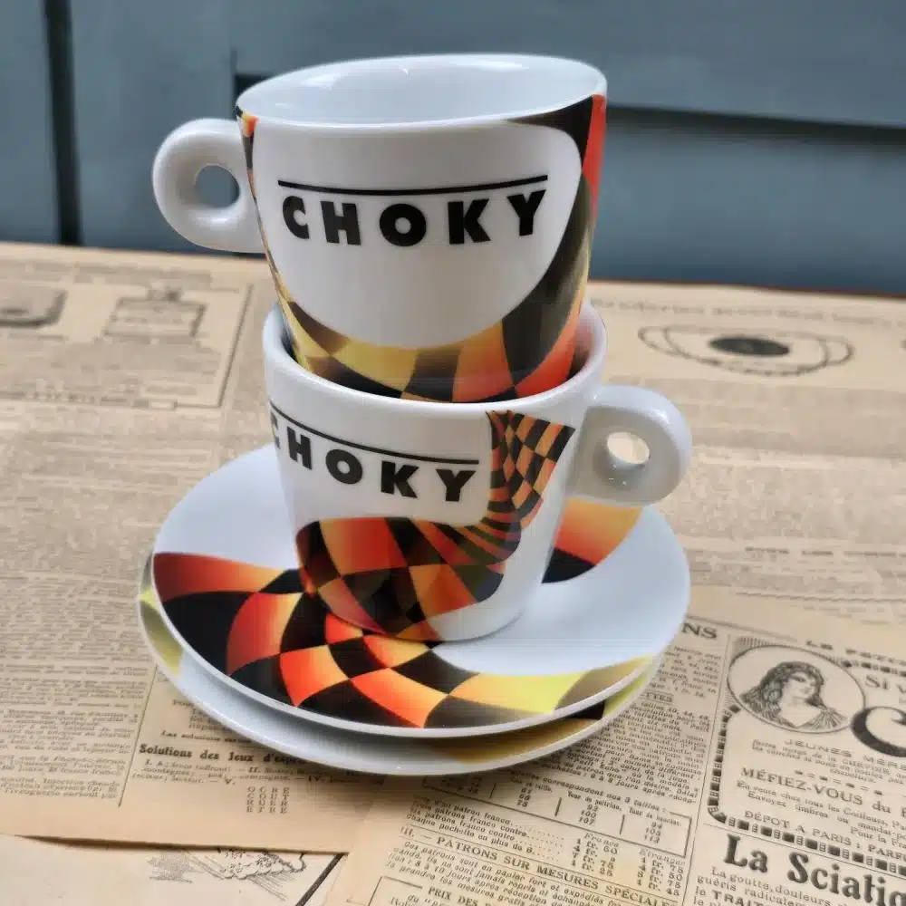 Lot de 2 tasses Choky vintage avec sous-tasses assorties, posé sur fond de journaux anciens.