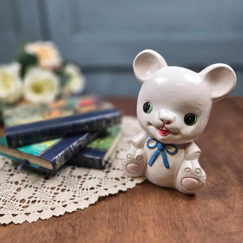 Tirelire ours vintage en céramique blanche avec nœud bleu, mise en scène sur une table avec des livres anciens